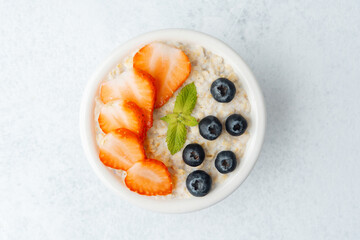 Top view of oatmeal with strawberries and blueberries on white background