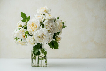 White roses bouquet in glass vase on white table with light background