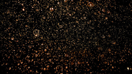 Glistening water droplets on dark surface with golden glow
