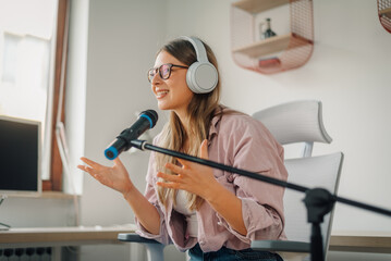 Young woman recording podcast from home office using microphone and headphones