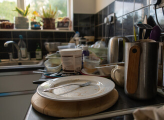 A messy and dirty kitchen with unwashed plates, cups and cutlery.