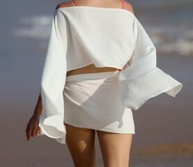A woman is walking on the beach wearing a white dress