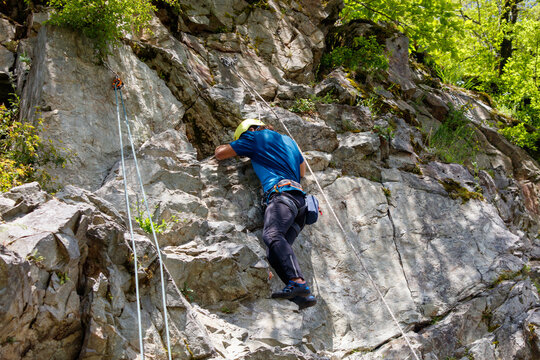 A man is climbing a rock wall with a yellow helmet on