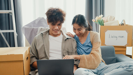 Young happy Asia couple sit on sofa couch use computer laptop online shopping furniture from...