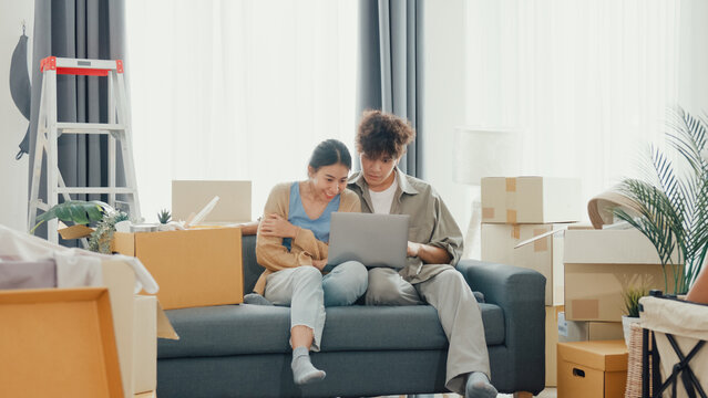 Young happy Asia couple sit on sofa couch use computer laptop online shopping furniture from decoration store in living room at home. Husband wife move new house, Apartment Rent And Ownership Concept. - Powered by Adobe