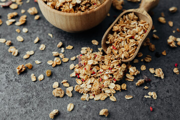 Granola bowl and scoop with scattered cereal on dark background