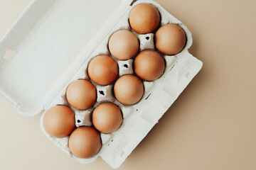 Brown eggs in white carton on beige background flat lay