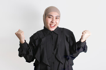 Happy woman in hijab cheering with clenched fists, expressing joy, success, and confidence....