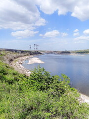 Panorama of the Khortytsia coast of the Dnieper under the rays of the midday sun against the background of a dam and power lines on the horizon.