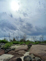 A celestial panorama from the rocky coast of the Dnieper River of heavy rain clouds through which the rays of the midday sun are breaking through.