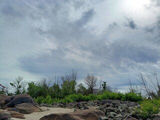 A celestial panorama from the rocky coast of the Dnieper River of heavy rain clouds through which the rays of the midday sun are breaking through.