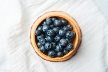 Fresh blueberries in a wooden bowl on a white cloth surface