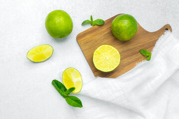 Fresh limes arranged on a wooden cutting board with mint leaves nearby