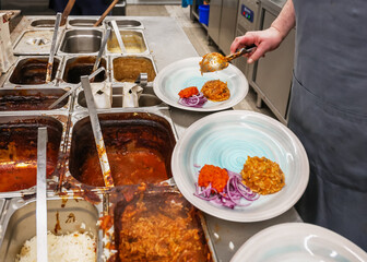 Chef plating food in a restaurant kitchen. Fresh rice with sauce, red pepper and onion being served in a commercial catering environment.