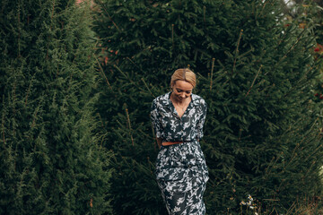 A young adult woman walks in the park among the fir trees