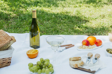Picnic with wine, fruits and cheese in orchard grass for concepts of friendship, lifestyle and outdoor dining