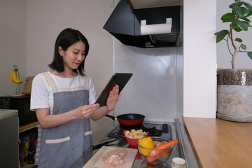 キッチンでタブレットを見ながら料理をする女性