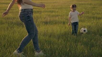 Little child runs across the green football field playing football at sunset in the sky, kid kicks...