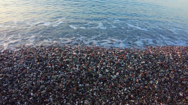 4K Close-up of gentle waves with a sound washing over colorful pebbled beach shore at Konyaalti in Antalya, Turkey. The clear Mediterranean water calmly meets the shoreline in the early morning light