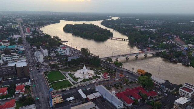 Aerial view of Surat Thani, Thailand, featuring the City Pillar Shrine, Tapi River, and city bridges under a vast sky at dusk.