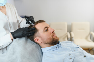 Man getting hair treatment at beauty salon, having mesotherapy session. Female therapist hands in...