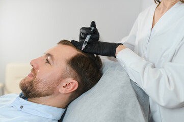 Mesotherapy for hair. Attractive man receiving injections in his head. Man having mesotherapy...