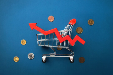 A shopping cart with a red zigzag arrow and scattered coins on a blue background. Top view, flat...