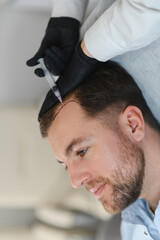 Fototapeta premium Man getting hair treatment at beauty salon, having mesotherapy session. Female therapist hands in protective gloves making injection with syringe