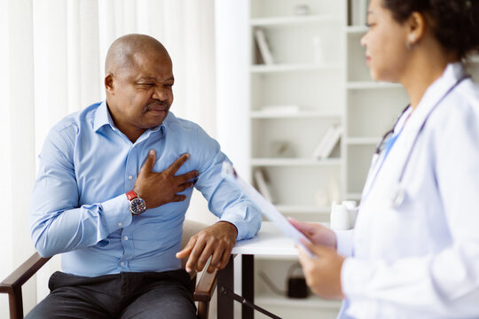 Male patient holding his chest in visible pain while talking with female doctor, possibly indicating a serious medical issue during consultation, closeup - Powered by Adobe