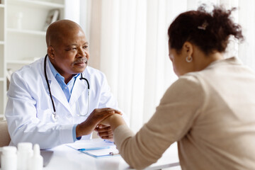 Doctor reassures pregnant patient by holding her hand during emotional consultation in clinic....