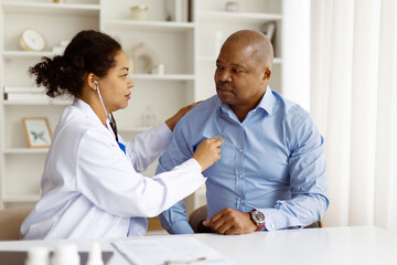 Black female doctor listening to male patients chest using stethoscope during clinical checkup....