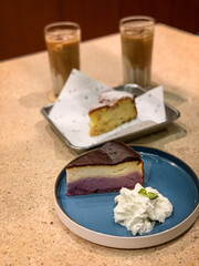 Delicious ube velvet cheesecake with whipped cream and a slice of moist cheesecake, served with refreshing iced lattes. Perfect dessert and coffee pairing.