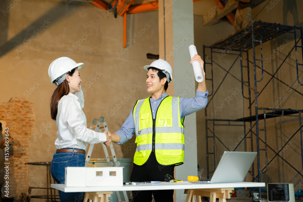 Poster construction engineer and architect shake hands over blueprints and scale model in an unfinished bui