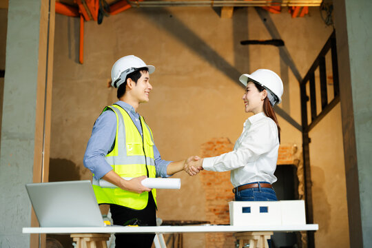 Construction engineer and architect shake hands over blueprints and scale model in an unfinished building interior, sealing partnership and trust
