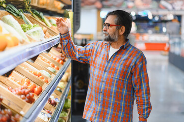 Stylish senior man in red shirt choosing vegetables and fruits at supermarket