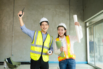 Two construction professionals in hard hats and safety vests raise their fists in celebration over...