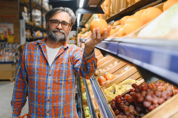 Stylish senior man in red shirt choosing vegetables and fruits at supermarket