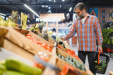 Stylish senior man in red shirt choosing vegetables and fruits at supermarket