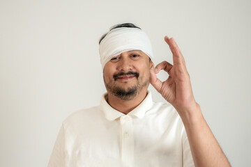Young man with bandaged head giving thumbs up, smiling to show he’s fine after an accident.
