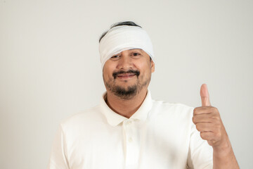 Young man with bandaged head giving thumbs up, smiling to show he’s fine after an accident.