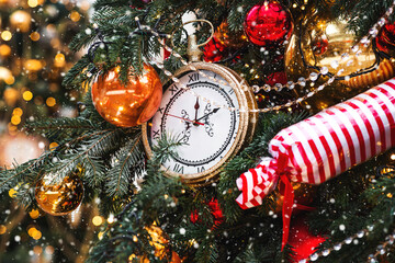 Golden retro clock on a Christmas tree. The clock hands show 12 o'clock. Beautiful background for...