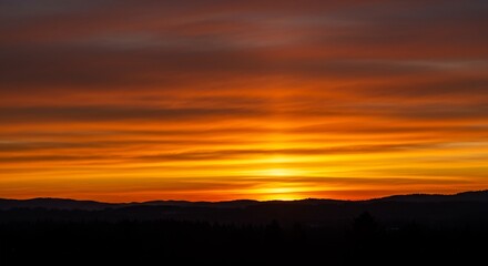 Obraz premium Vibrant Orange Sunset over Silhouetted Mountain Range and Forest Landscape