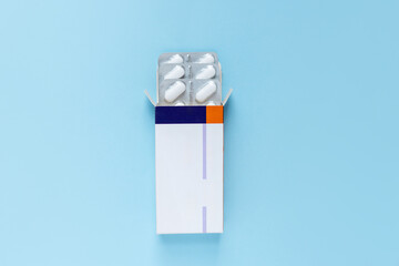 Opened box of white capsules in blister packs on blue background. Medical supplies for treatment,...