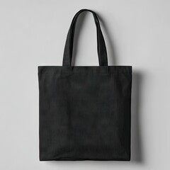 A plain black cotton tote bag with two handles hangs against a light grey backdrop