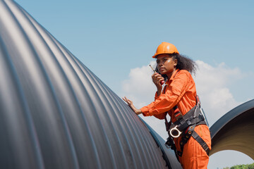 A black female mechanical engineer in a safety uniform inspects and inspects piping systems for a...