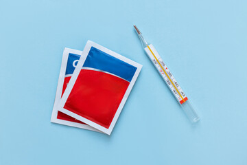 Medical still life with two red-blue medicine powder sachets and a glass thermometer on a light...