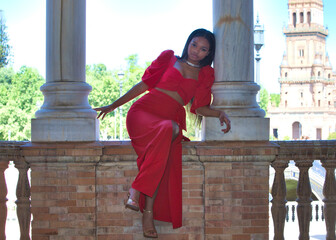 african woman, with long brown hair, young and beautiful dressed in an elegant red dress sitting...