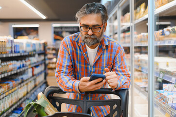 Senior Man doing grocery shopping at the supermarket, he is using apps on his smartphone