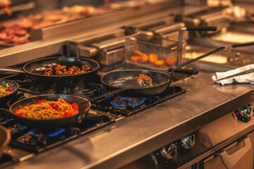 Multiple dishes cooking on gas burners in a busy professional kitchen. Pasta, vegetables, and meats...