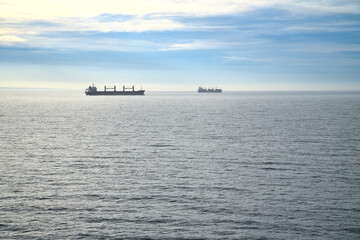 Two cargo ships glide across a calm sea under a clear sky. Minimalist seascape.